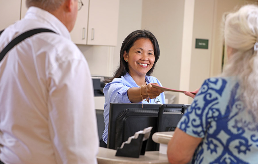 A smiling receptionist handing patients a pamphlet.